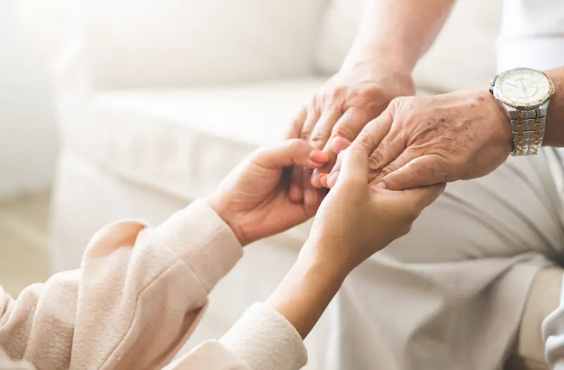 A caregiver holding the hands of an older adult